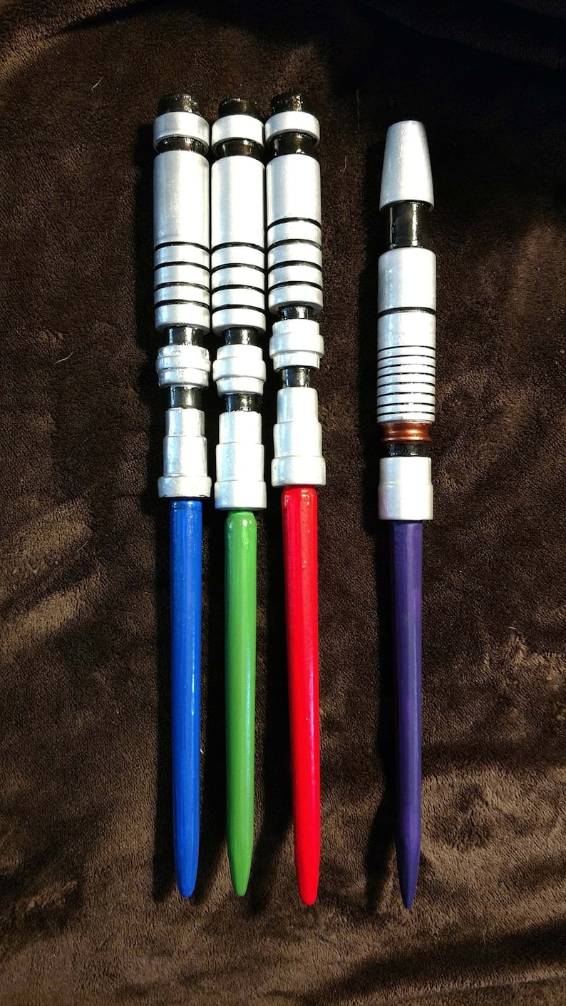 Op de afbeelding: Vier zilveren lightsaber-handvatten met zwarte accenten. De handvatten hebben blauwe, groene, rode en paarse bladen.