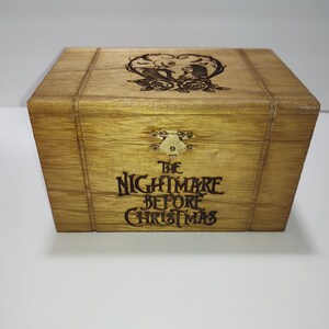 May include: A wooden box with a hinged lid and a brass latch. The box is decorated with an engraved design of Jack Skellington and Sally from the movie "The Nightmare Before Christmas". The text "The Nightmare Before Christmas" is also engraved on the front of the box.