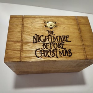 May include: A wooden box with a hinged lid and a brass latch. The box is decorated with a black burned-in design that reads "The Nightmare Before Christmas".