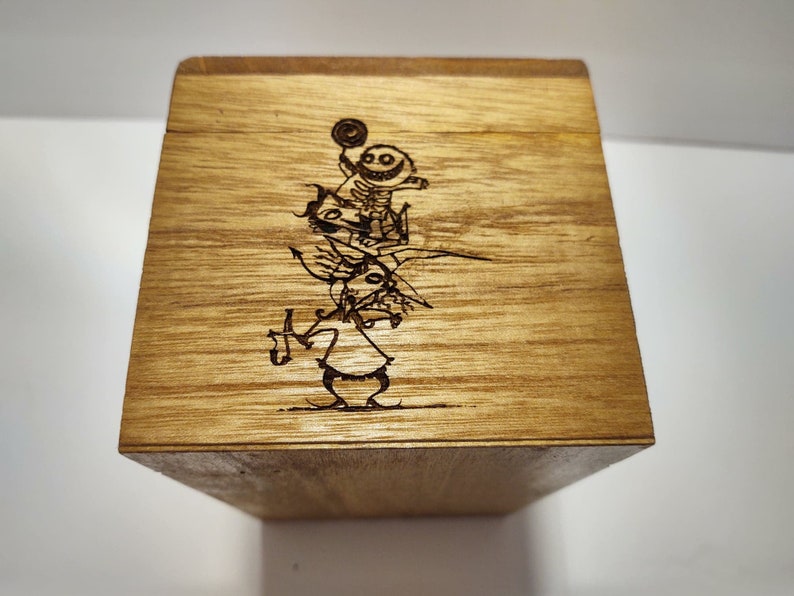 May include: A wooden box with a laser-engraved image of three characters from the movie "The Nightmare Before Christmas". The characters are Jack Skellington, Sally, and Oogie Boogie.