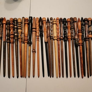 May include: A collection of 28 wooden wands, each with a unique design and finish. The wands are arranged in a row on a white surface.