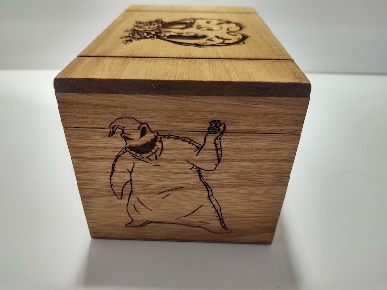 May include: A wooden box with a hinged lid. The box is decorated with an engraved image of a character from the movie "The Nightmare Before Christmas".