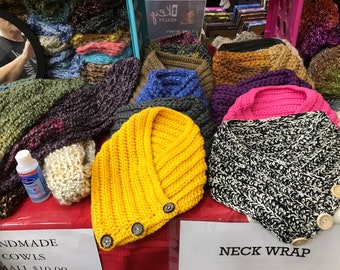 Puede incluir: Exhibición de cuellos y bufandas hechas a mano en varios colores y patrones. Los cuellos incluyen uno amarillo brillante con botones de madera, una bufanda con estampado en blanco y negro, y otros en rosa, azul y morado. El texto "NECK WRAP" es visible.