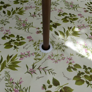 May include: A white tablecloth with a floral pattern featuring various herbs and their names. The tablecloth has a hole in the centre for an umbrella pole.