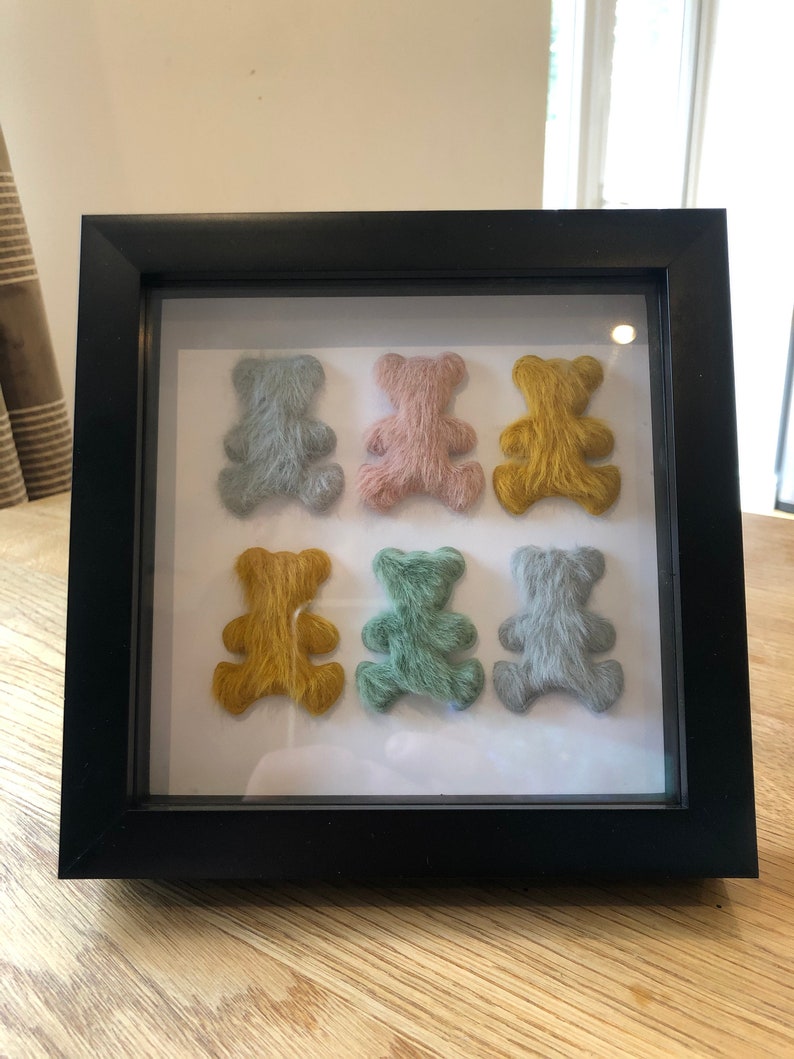 May include: A framed display of six small, fuzzy teddy bears in a variety of colors, including blue, pink, yellow, and green. The bears are arranged in two rows of three.