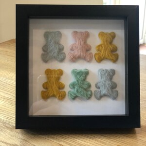 May include: A framed display of six small teddy bears, each with a different color of fuzzy fur. The bears are arranged in two rows of three, with the top row featuring light blue, pink, and yellow bears. The bottom row features yellow, green, and light blue bears.