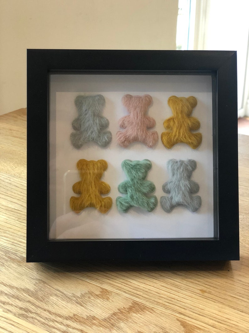 May include: A framed display of six small teddy bears, each with a different color of fuzzy fur. The bears are arranged in two rows of three, with the top row featuring light blue, pink, and yellow bears. The bottom row features yellow, green, and light blue bears.