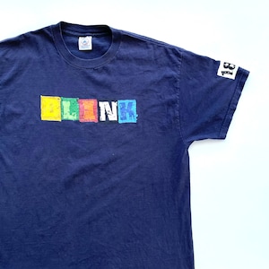 May include: A navy blue t-shirt with a colorful "blink 182" logo printed on the front. The logo is made up of individual squares with each letter in a different color.