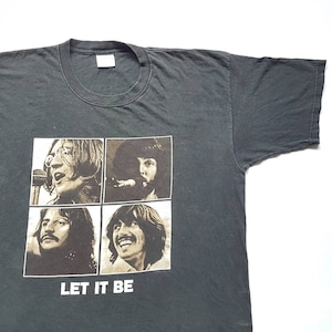 May include: Black t-shirt with a vintage-style image of the Beatles from the album "Let It Be". The image shows four black and white photos of the band members in a grid pattern. The text "Let It Be" is printed below the image.