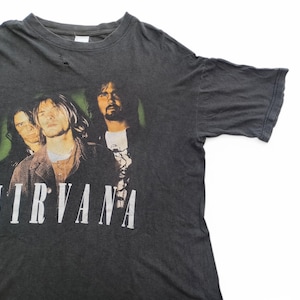May include: A black t-shirt featuring a faded image of the band Nirvana. The band members are pictured in black and white, with the band's name printed in white letters below the image.