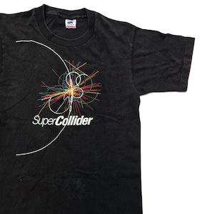 May include: A black short-sleeve t-shirt featuring a graphic of colorful particle collision lines and the white text SuperCollider. The design includes a large white curved line extending across the chest area, set against the solid black fabric.