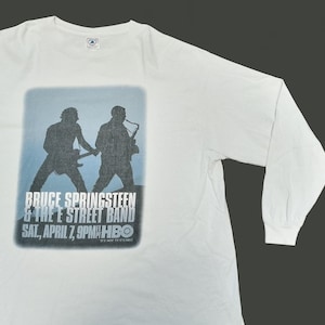 May include: White long-sleeve shirt featuring a blue and white graphic of Bruce Springsteen & The E Street Band. The graphic includes silhouettes of two band members and the text "BRUCE SPRINGSTEEN & THE E STREET BAND SAT., APRIL 7, 9PM HBO".