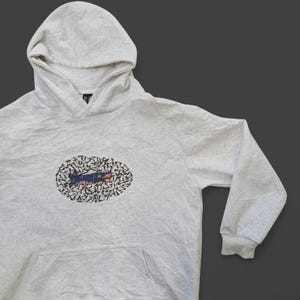 May include: A light grey hooded sweatshirt with a graphic print of a black and white design inside a circle. The design features a blue and orange shape with a black outline.