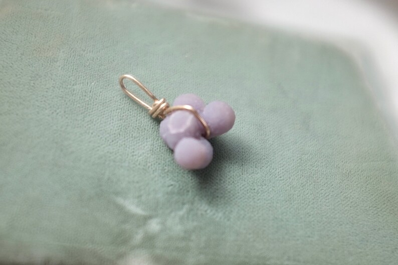May include: A silver wire wrapped pendant featuring three lavender-colored, irregularly shaped stones.
