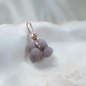 May include: A silver wire wrapped around a cluster of three lavender-colored agate stones, forming a pendant.