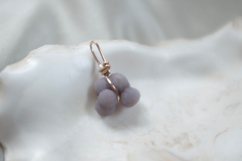May include: A silver wire wrapped around a cluster of three lavender-colored agate stones, forming a pendant.