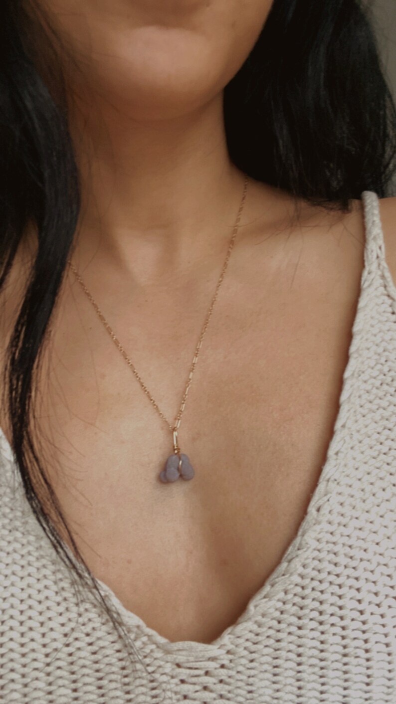 May include: A gold chain necklace with a pendant made of two small, light purple stones.