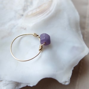 May include: A delicate gold ring with a single, faceted, purple gemstone.