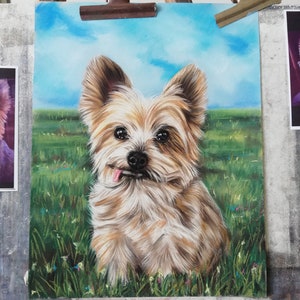 May include: A pastel drawing of a small, light brown and white dog with a long, fluffy coat. The dog is sitting in a field of green grass with blue sky in the background. The dog has its tongue sticking out and is looking directly at the viewer.
