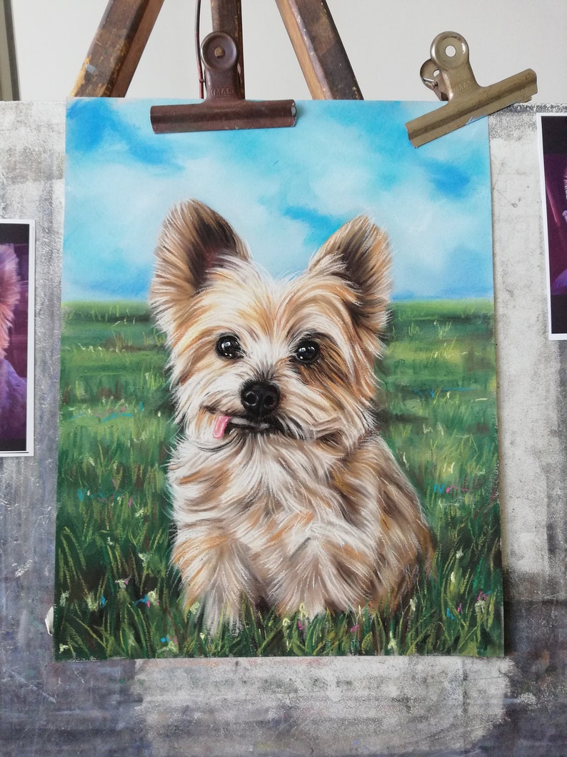 May include: A pastel drawing of a small, light brown and white dog with a long, fluffy coat. The dog is sitting in a field of green grass with blue sky in the background. The dog has its tongue sticking out and is looking directly at the viewer.