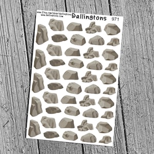 May include: A sheet of stickers featuring various gray rock illustrations. The rocks vary in size and shape, with some appearing as individual stones and others as clusters. The stickers are designed for crafting or planning purposes.