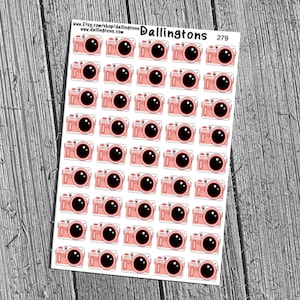 Könnte beinhalten: Blatt mit Aufklebern mit einem sich wiederholenden Muster aus rosa Kameras mit schwarzen Objektiven. Die Aufkleber befinden sich auf weißem Hintergrund, mit dem Text "Dallingtons" und "279" sichtbar. Der Hintergrund ist eine Holzoberfläche.