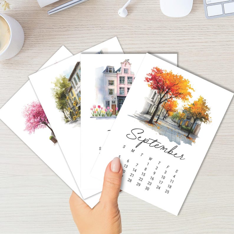Puede incluir: Un conjunto de cuatro tarjetas de calendario rectangulares con ilustraciones en acuarela de edificios de estilo europeo y &aacute;rboles estacionales. La tarjeta superior muestra el mes de septiembre con una escena callejera con follaje oto&ntilde;al naranja y amarillo.