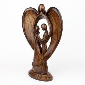 May include: A wooden sculpture of a couple standing inside a heart-shaped frame. The sculpture is made of dark brown wood and has a smooth finish.