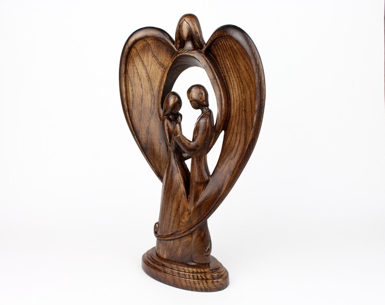 May include: A wooden sculpture of a couple standing inside a heart-shaped frame. The sculpture is made of dark brown wood and has a smooth finish.