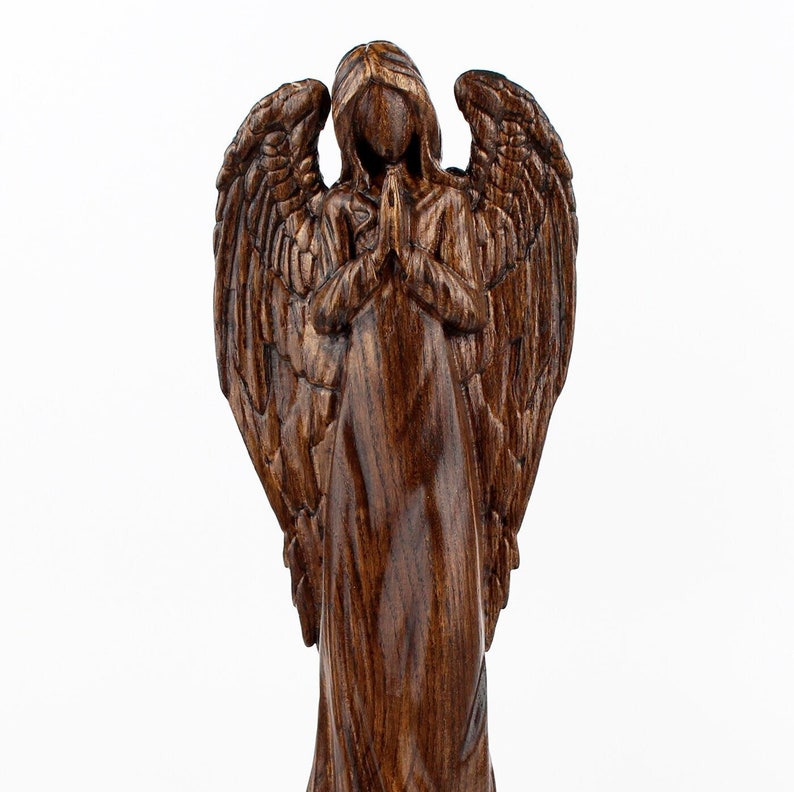 May include: A wooden angel figurine with wings outstretched and hands clasped in prayer. The angel is carved from dark wood with a rich brown finish.