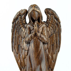 May include: A dark brown wooden angel figurine with wings outstretched and hands clasped in prayer. The angel is carved in a realistic style with detailed features.