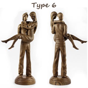 May include: A wooden sculpture of a couple embracing. The man is holding the woman in his arms. The sculpture is made of dark wood with a grain pattern. The sculpture is on a wooden base. Type 6.