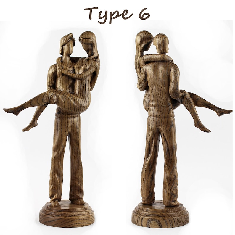 May include: A wooden sculpture of a couple embracing. The man is holding the woman in his arms. The sculpture is made of dark wood with a grain pattern. The sculpture is on a wooden base. Type 6.