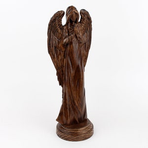 May include: A wooden angel figurine with wings outstretched and a flowing robe. The angel is carved from dark wood and has a detailed face.