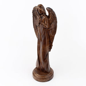 May include: A wooden angel figurine with wings outstretched, carved from dark brown wood. The angel is standing on a round base.
