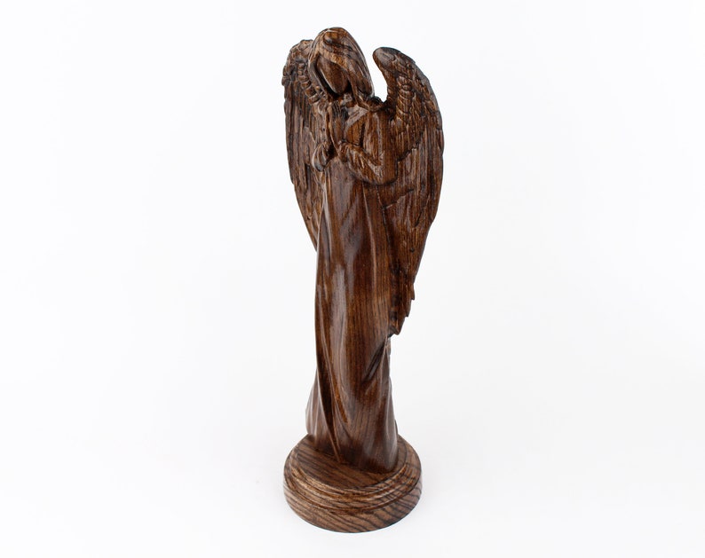 May include: A wooden angel figurine with wings outstretched, carved from dark brown wood. The angel is standing on a round base.