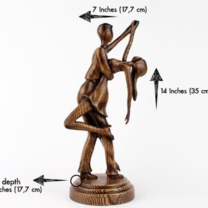 May include: A wooden sculpture of a couple dancing, the man holding the woman in a dip. The sculpture is 14 inches tall and 7 inches wide.
