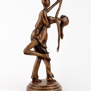 May include: A wooden sculpture of a couple dancing, the man holding the woman in a dip. The sculpture is dark brown and has a natural wood grain finish.