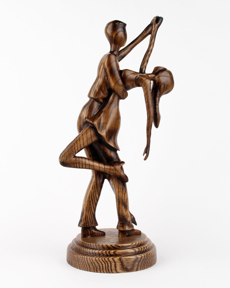 May include: A wooden sculpture of a couple dancing, the man holding the woman in a dip. The sculpture is dark brown and has a natural wood grain finish.