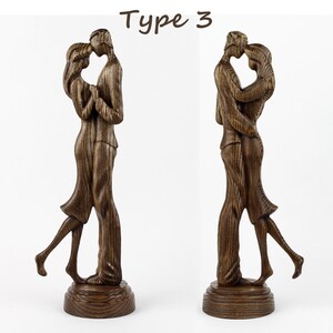 May include: A wooden sculpture of a couple embracing. The sculpture is made of dark wood and has a natural wood grain finish. The couple are standing on a wooden base.