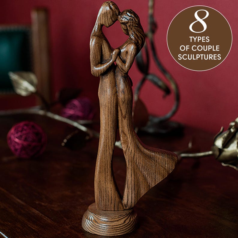 May include: A wooden sculpture of a couple embracing. The sculpture is made of dark brown wood and has a natural wood finish. The couple are standing on a small wooden base.