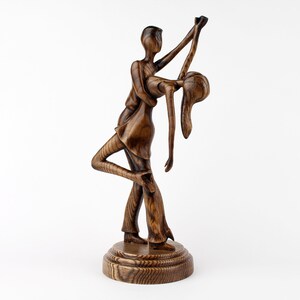 May include: A wooden sculpture of a couple dancing, the man is holding the woman in a dip, both are carved in a dark brown wood.