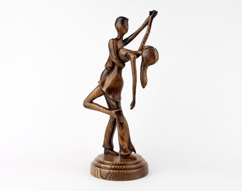 May include: A wooden sculpture of a couple dancing, the man is holding the woman in a dip, both are carved in a dark brown wood.