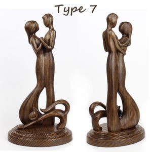 May include: A wooden sculpture of a couple embracing, with the woman's arm around the man's waist. The sculpture is dark brown and has a detailed wood grain pattern. The couple are standing on a base with a decorative design. The sculpture is labelled "Type 7".