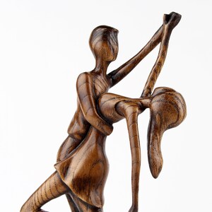 May include: A wooden sculpture of a couple dancing. The man is holding the woman in a dip, and they are both smiling. The sculpture is made of dark wood and has a rustic finish.