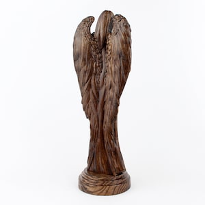 May include: A wooden angel sculpture with detailed wings and a rustic brown finish. The angel is standing on a round base.