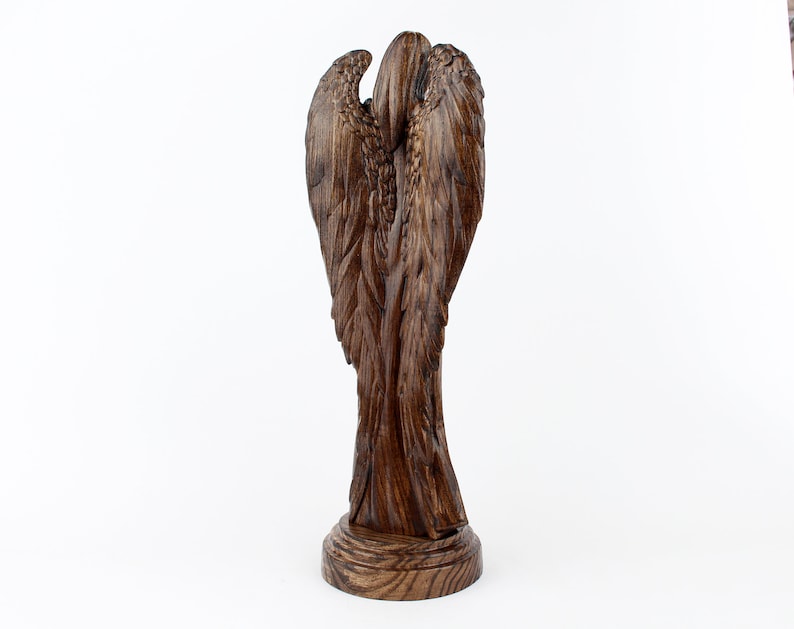 May include: A wooden angel sculpture with detailed wings and a rustic brown finish. The angel is standing on a round base.