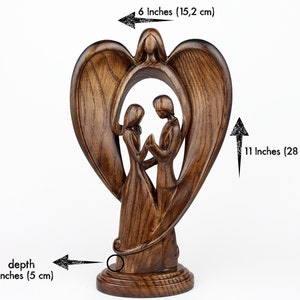 May include: A wooden sculpture of a couple standing inside a heart-shaped frame with angel wings. The sculpture is 11 inches tall, 6 inches wide, and 2 inches deep.