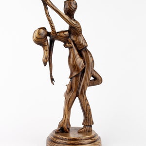 May include: A wooden sculpture of a couple dancing. The man is holding the woman in a dip, and they are both smiling. The sculpture is made of dark wood with a natural grain.