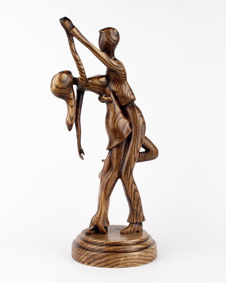 May include: A wooden sculpture of a couple dancing. The man is holding the woman in a dip, and they are both smiling. The sculpture is made of dark wood with a natural grain.